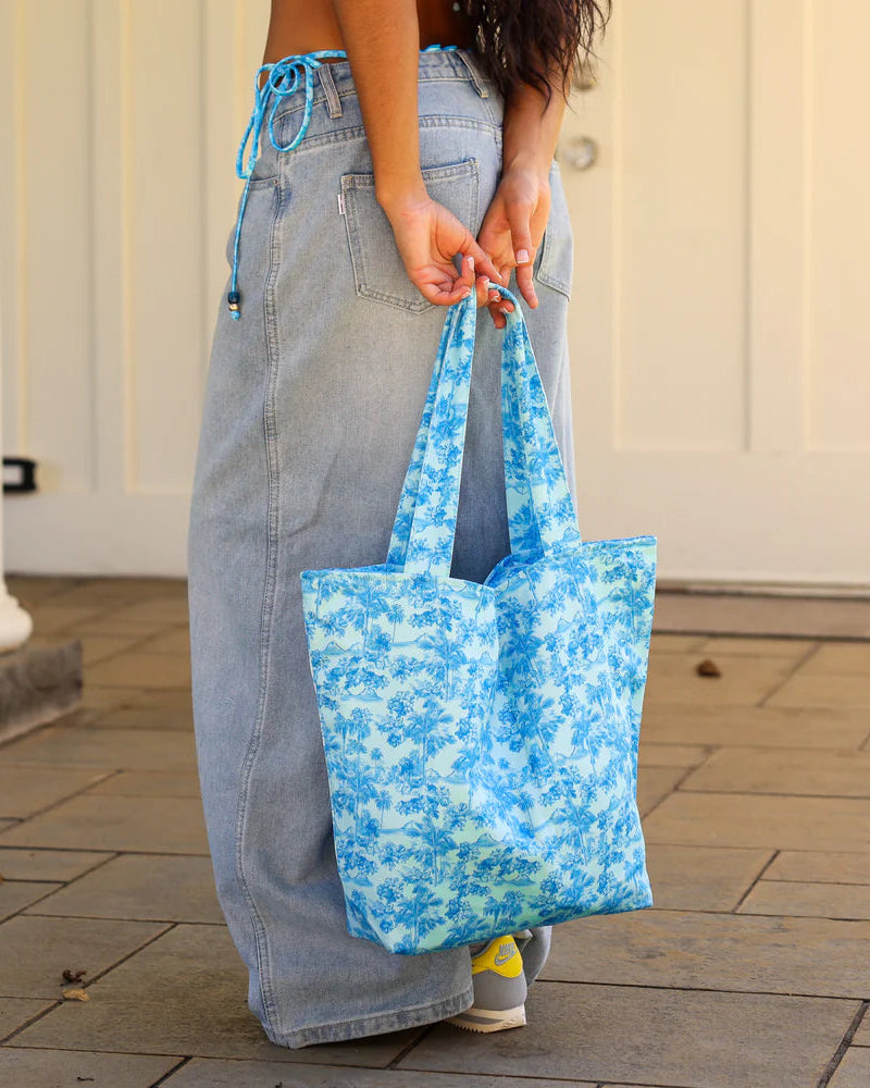 Person holding a blue floral tote bag on a paved surface.