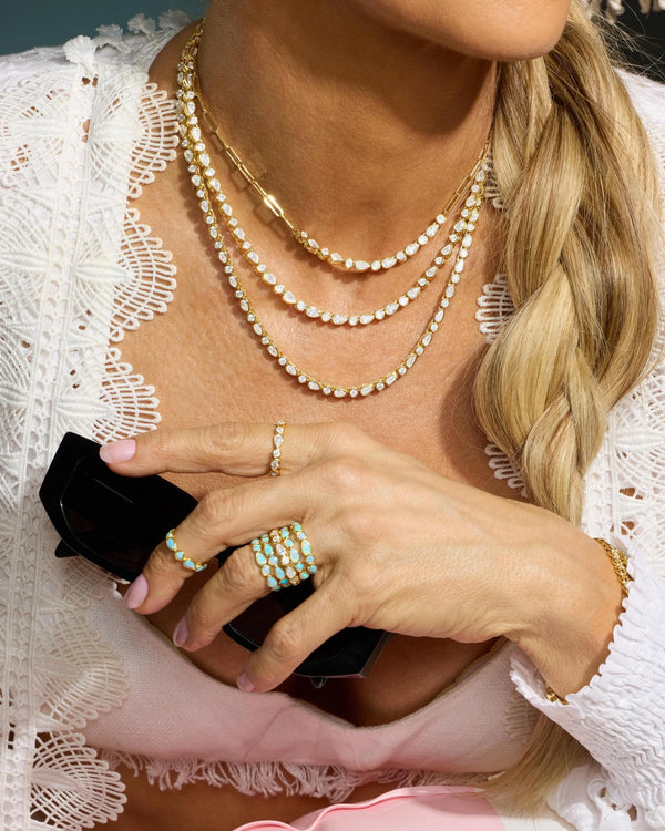 Person wearing multiple necklaces and rings, holding a phone with a white lace garment.