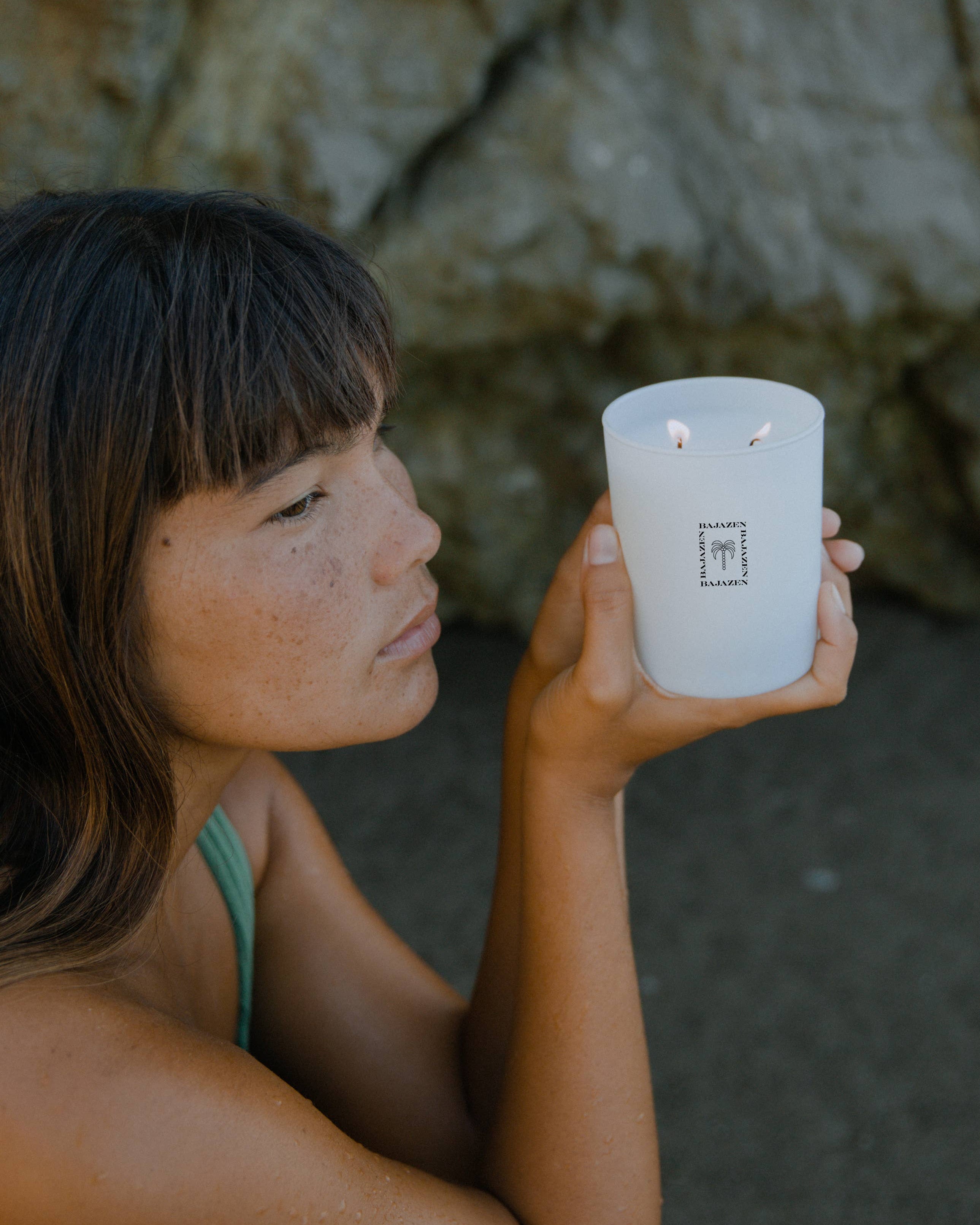 Person holding a white candle with a logo against a rocky background