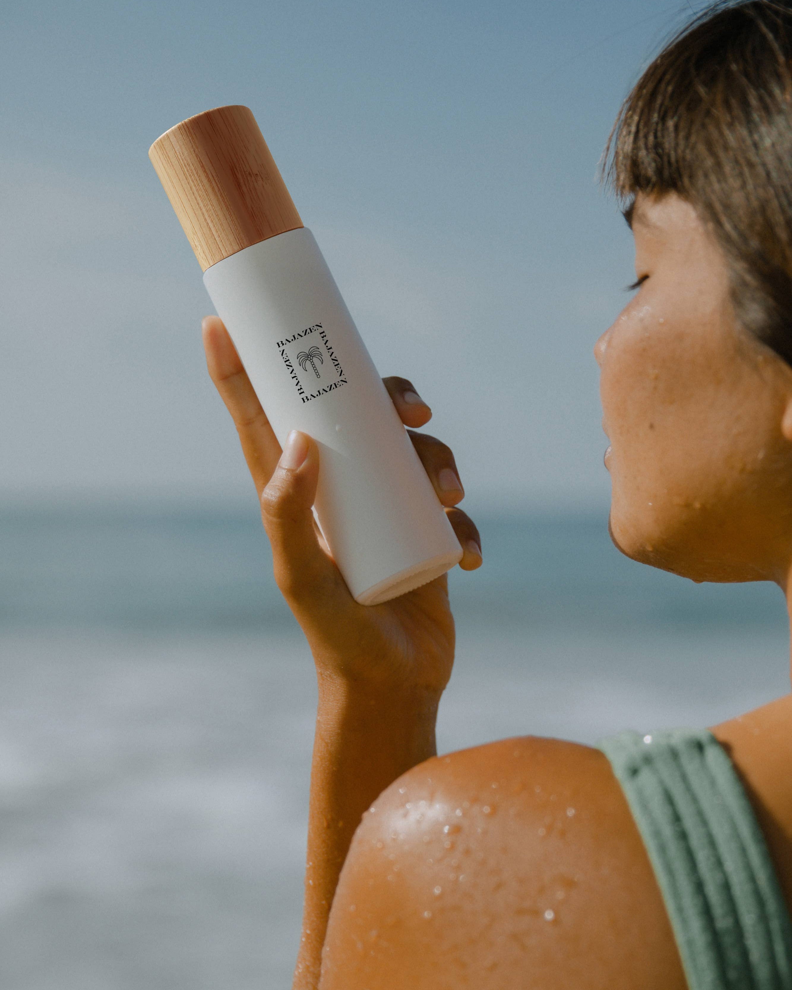 A person holding a white spray bottle with a wooden cap, labeled with 'Surf Haus' standing near a beach backdrop.