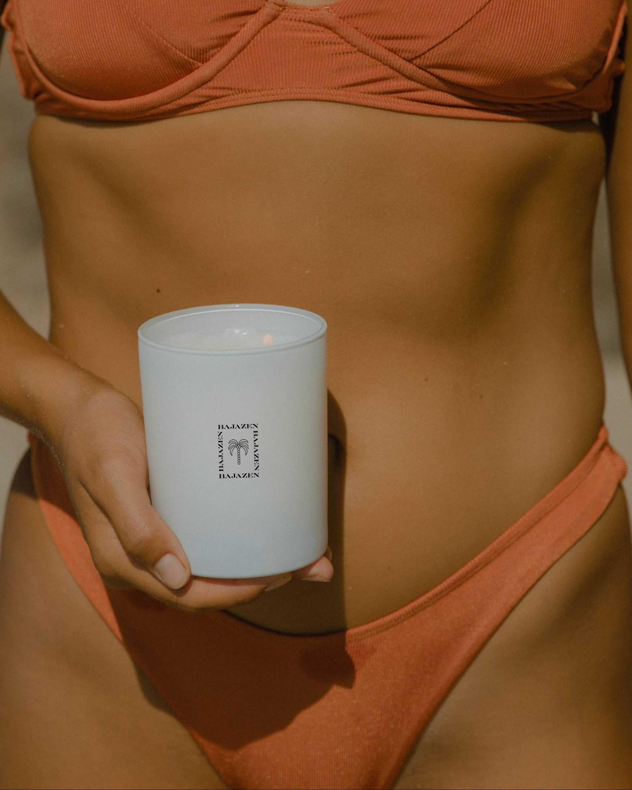 Person wearing an orange bikini holding a white candle with text on it.