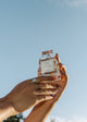 Hand holding a perfume bottle against a clear blue sky