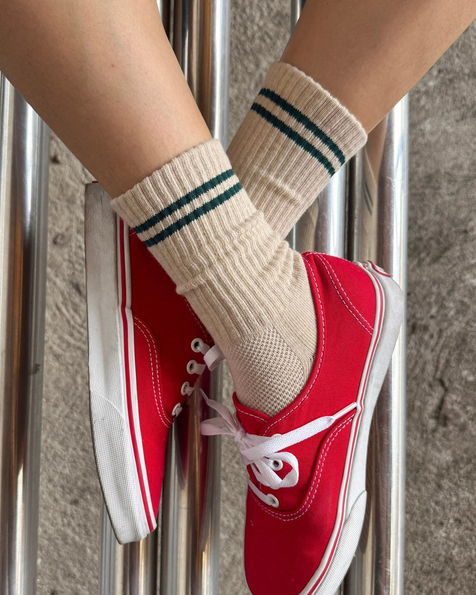 Beige socks with a green stripe on a person with red sneakers on. Showcasing Le Bon Shoppe socks. 
