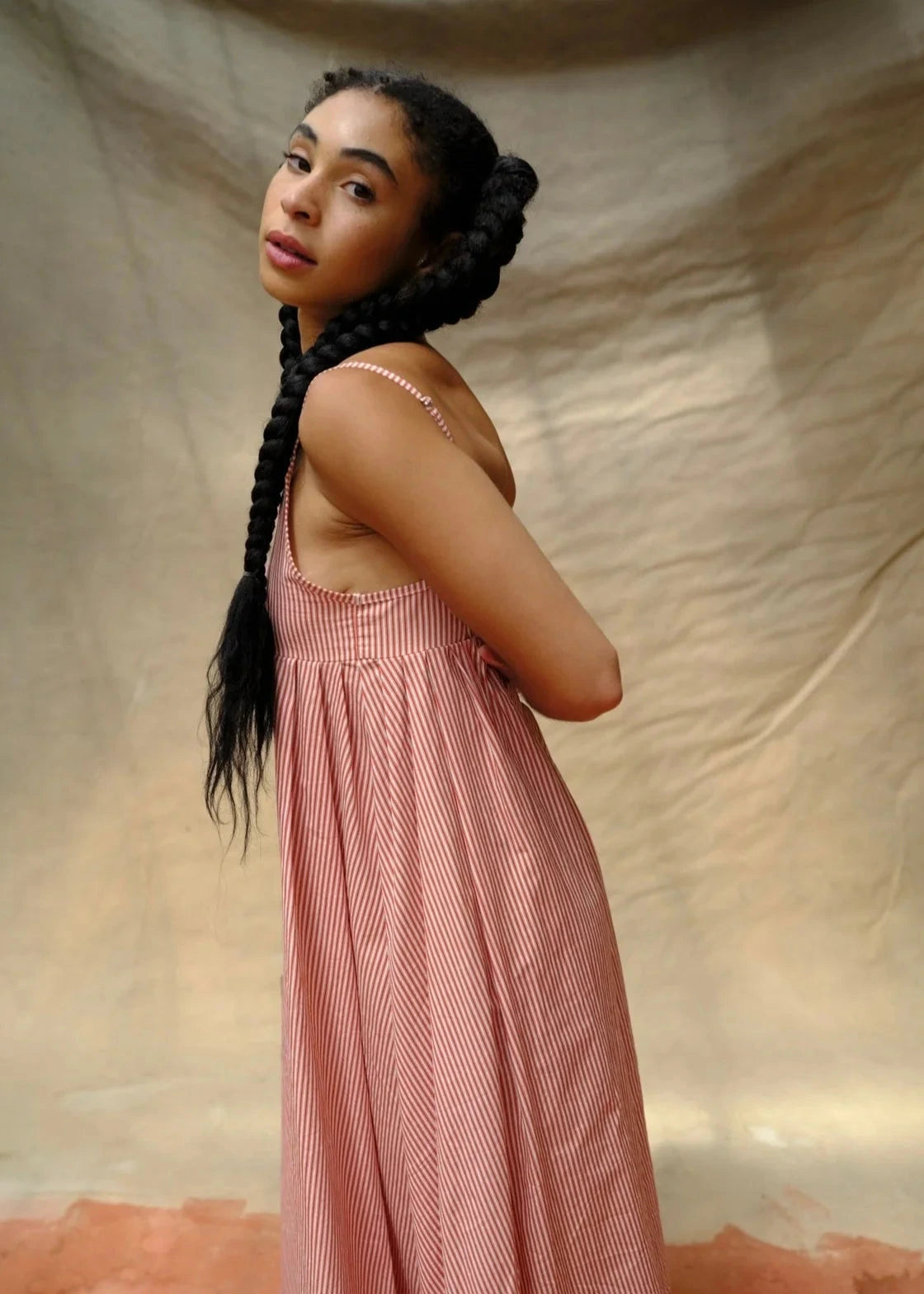 Woman in a pink dress standing against a beige fabric background