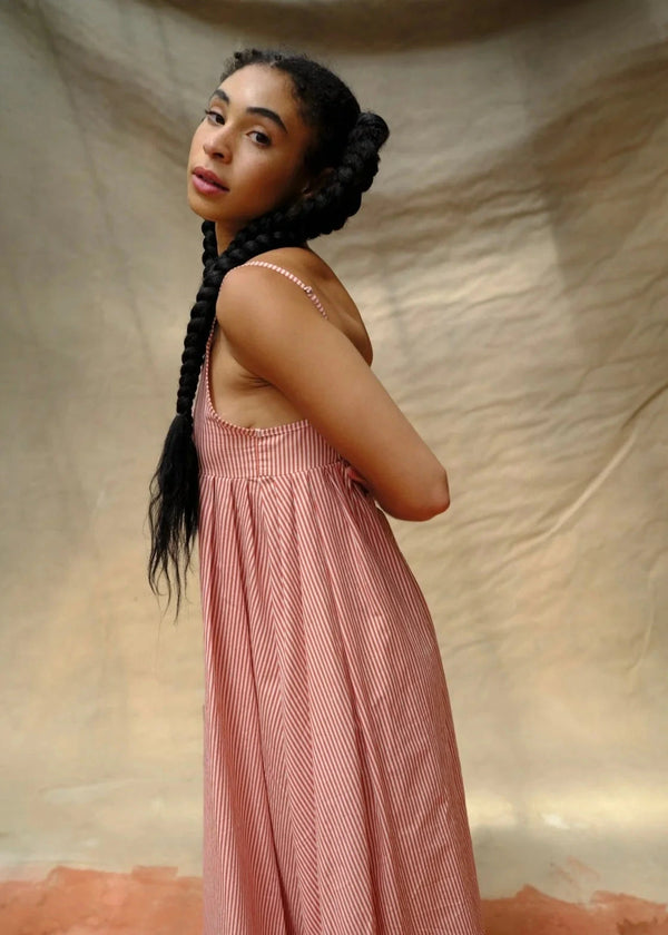Woman in a pink dress standing against a beige fabric background