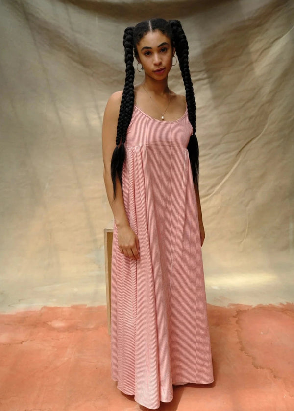 Woman in a pink dress with braided hair standing against a beige backdrop