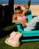 Woman in a pink bikini sitting on a teal chair by the beach