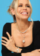 Woman wearing jewelry including a necklace, rings, and bracelets against a blue background