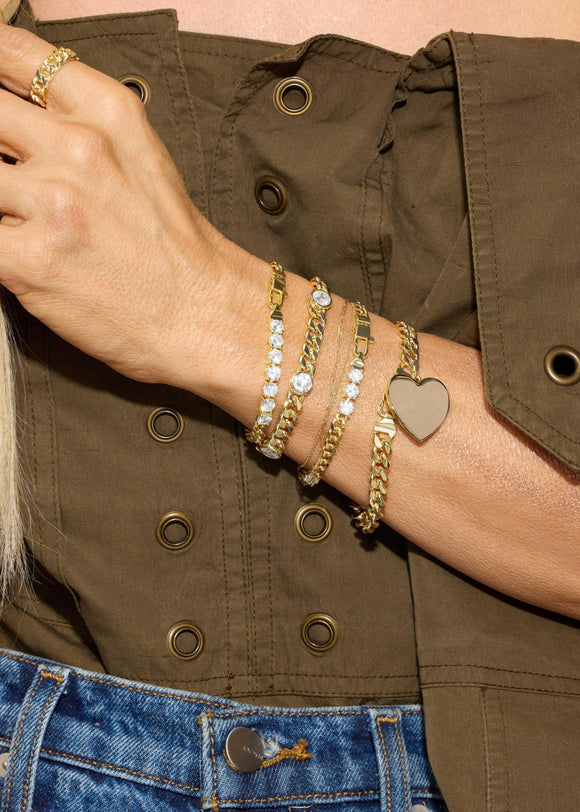 Close-up of a person's wrist wearing multiple gold bracelets with different designs, against a background of a green jacket and blue jeans.