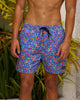 Person wearing colorful floral swim shorts standing in front of plants.