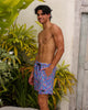 Man wearing colorful swim shorts standing outdoors with plants and a decorative door in the background