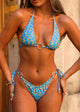 Woman wearing a blue floral bikini standing against a neutral wall.