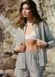 Woman wearing a striped shirt and shorts set against a stone wall.
