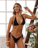 Woman in a black bikini standing next to a wooden ladder with flowers in a bright room.
