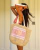 Woman holding a straw bag with a shell design against a neutral background