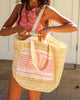 Woman holding a woven bag with a pink and white patterned top.